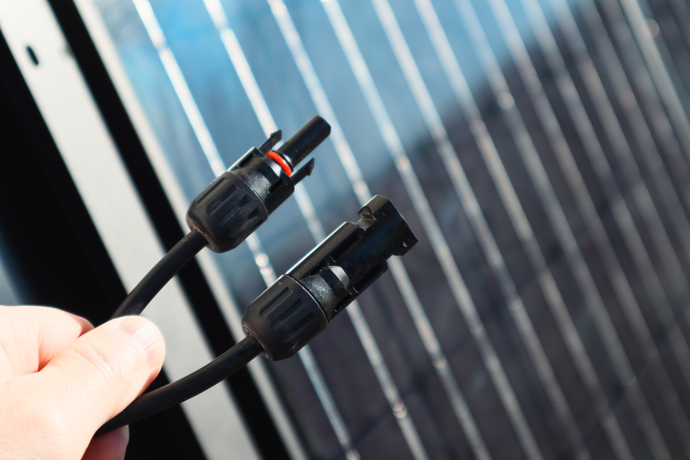 A pair of MC4 solar connectors held in front of a photovoltaic panel