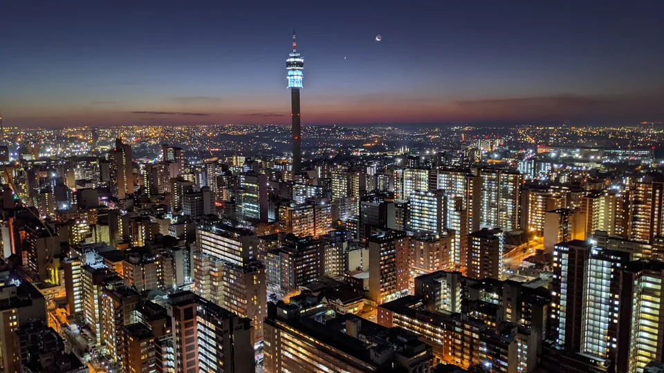 Johannesburg skyline at dusk with a tall tower and illuminated buildings beneath a blue and orange sky
